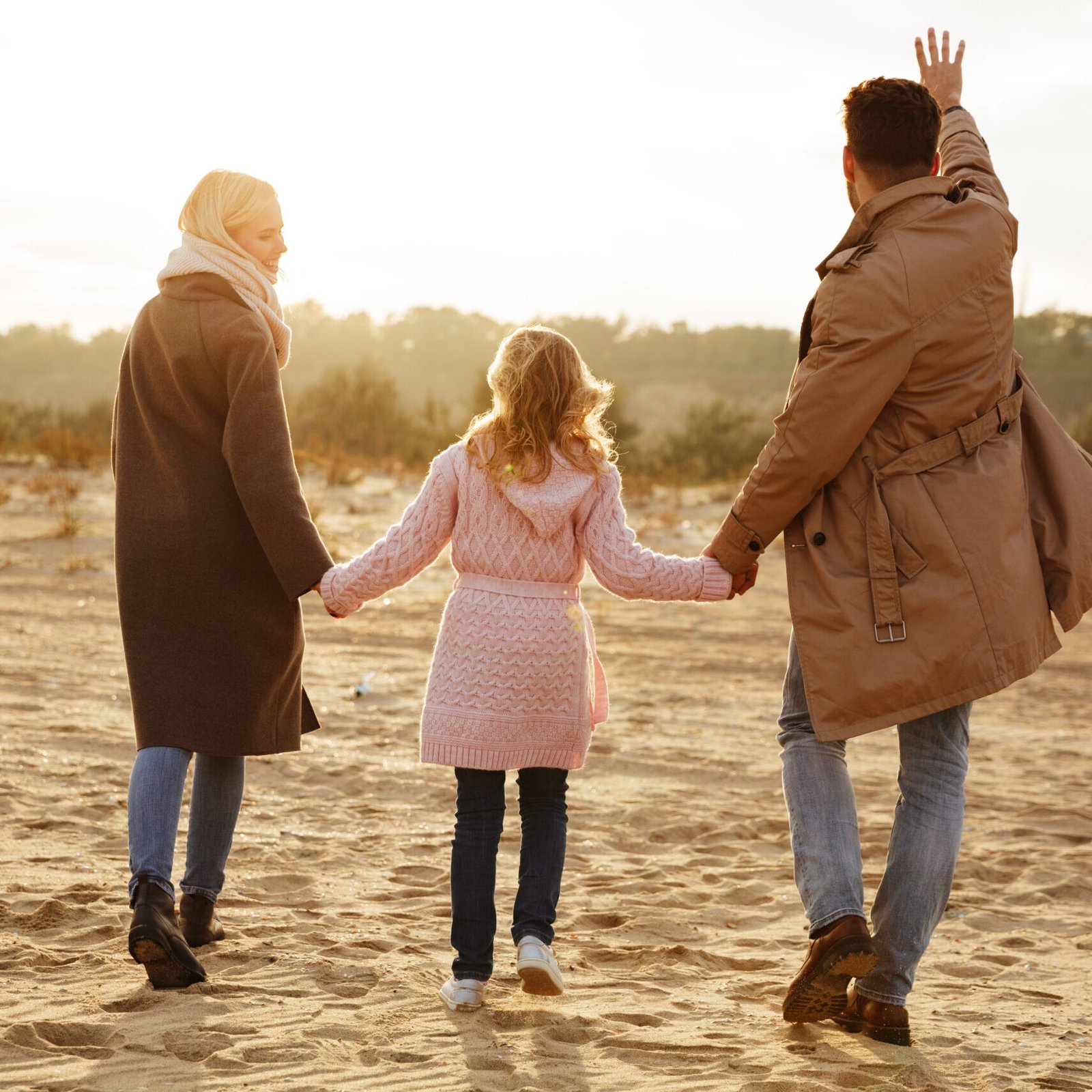 Portrait of a cheerful family with a little daughter having fun while walking along the beach together holding hands